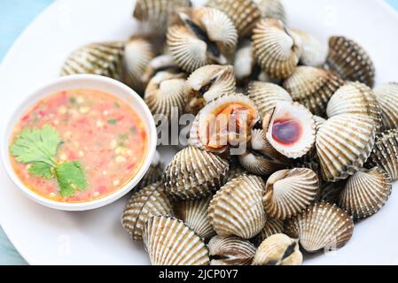 Herzmuscheln auf weißem Teller mit Meeresfrüchte-Sauce auf dem Tischhintergrund, frische rohe Schalentiere Blut Herzmuschel Ozean Gourmet Meeresfrüchte im Restaurant Stockfoto