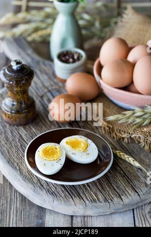 Nahaufnahme eines in Scheiben geschnittenen gekochten Eies auf einem kleinen Teller mit anderen rohen Eiern dahinter. Stockfoto