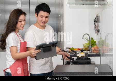 Junges Paar kocht und bereitet Essen nach einem Rezept auf einem Tablet-Computer in der Küche zu Hause zu Stockfoto