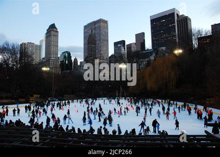 Eine große Menge Schlittschuhläufer genießt es, an einem Wintertag die Wollman Rink im Central Park unter der Skyline von New York City zu nutzen Stockfoto