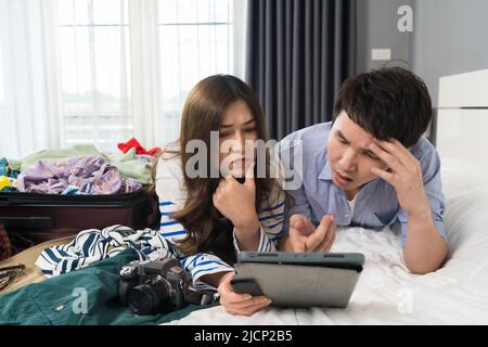 Gestresstes Paar mit Tablet und packen Kleidung in Koffer auf einem Bett zu Hause, Urlaub Reisekonzept Stockfoto