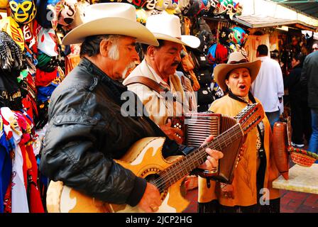 Drei Sänger und Mariachi-Musiker unterhalten ein Publikum, das traditionelle mexikanische Volkslieder in El Pueblo, einem Marktplatz in Los Angeles, singt Stockfoto