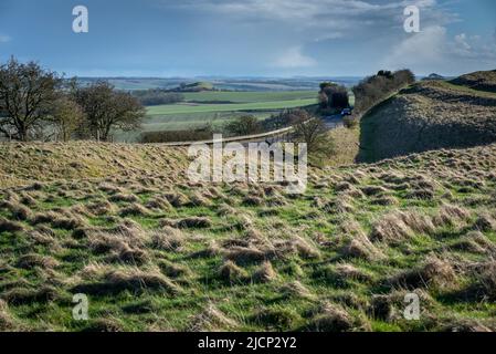 Ein entferntes Auto fährt an einem sonnigen Winternachmittag auf einer Landstraße durch die Landschaft von Wiltshire. Stockfoto