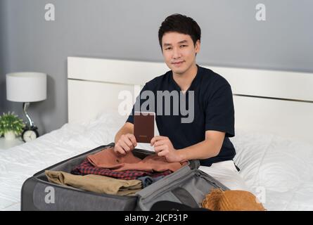 Junger Mann, der Passpord vorbereitet und Koffer auf dem Bett zu Hause verpackt, Urlaubsreisekonzept Stockfoto