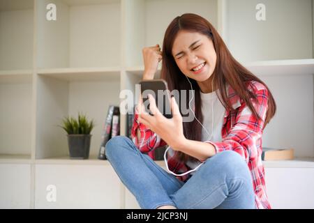 Fröhliche Teenager asiatische weibliche College-Student mit Smartphone, Musik hören oder Video-Anrufe mit ihren Freunden. Stockfoto
