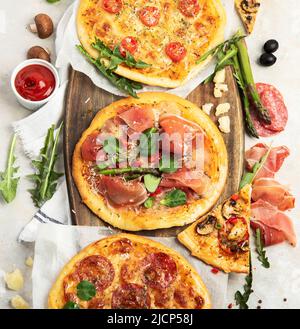 Verschiedene Arten von italienischer Pizza - Margherita, Pepperoni, Schinken, Pilze mit Basilikum, Tomaten, Olivenöl und Käse auf weißem Hintergrund. Draufsicht. Stockfoto