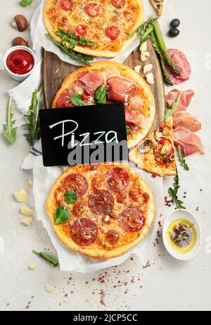 Verschiedene Arten von italienischer Pizza - Margherita, Pepperoni, Schinken, Pilze mit Basilikum, Tomaten, Olivenöl und Käse auf weißem Hintergrund. Draufsicht. Stockfoto