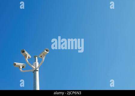 Drei CCTV-Überwachungskameras, die an einem Pfosten montiert sind, isoliert gegen einen blauen Himmel Stockfoto