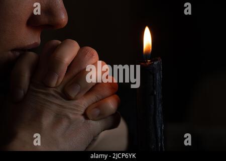 Ein junges ukrainisches Mädchen betet in der Ukraine in der Nähe einer Kerze für die Ukraine, ein Mädchen goss Kerzen in der dunklen Nahaufnahme Stockfoto