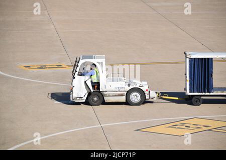 Ein Mitarbeiter von United Airlines, der einen Traktor fährt und einen leeren Gepäckwagen am Dallas Fort Worth International Airport (DFW Airport) zieht Stockfoto