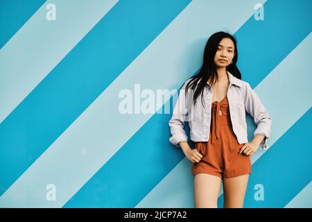 Selbstbewusste junge asiatische Frau, die die Kamera anschaut, während sie im Freien posiert. Stockfoto