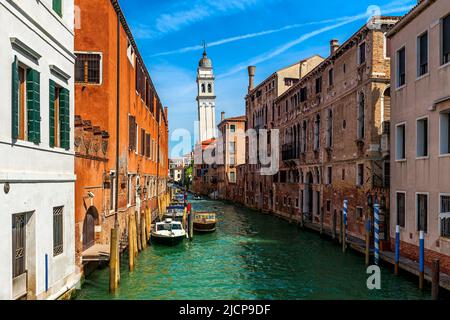 Blick auf Boote auf schmalen Kanal zwischen alten Häusern als schiefer Glockenturm im Hintergrund in Venedig, Italien. Stockfoto