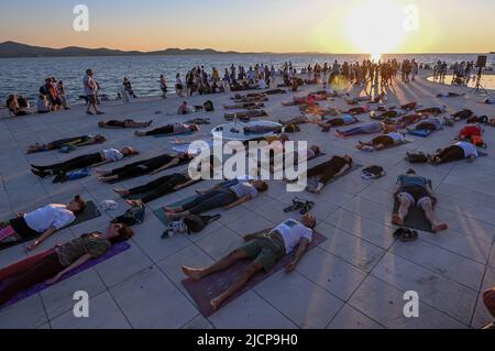 Menschen üben Yoga bei Sonnenuntergang an der Meeresorgel, um den Internationalen Yoga-Tag in Zadar, Kroatien, am 14. Juni 2022 zu feiern. Foto: Dino Stanin/PIXSE Stockfoto