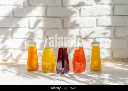 Reihe von Glasflaschen mit verschiedenen Säften gegen weiße Ziegelwände Stockfoto