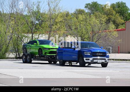 Ein blauer Dodge RAM Pick-up-Truck zieht einen grünen Sportwagen auf einem Anhänger Stockfoto