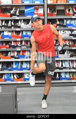 Generation Z (Gen Z) junger Mann in einem Schuhgeschäft, der Schuhe ausprobiert Stockfoto