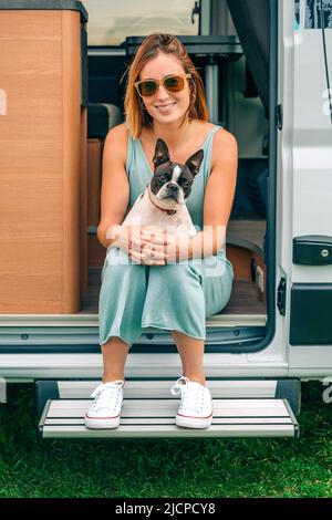 Frau, die während einer Reise mit ihrem Hund an der Tür ihres Wohnwagens sitzt Stockfoto