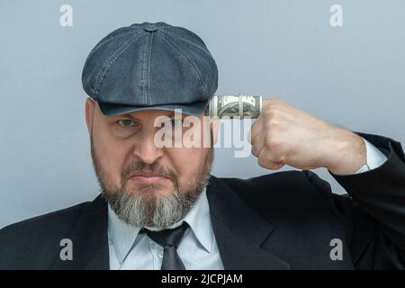 Der Mann legte seinen Finger in seinen Tempel. Der Finger ist in eine Dollarnote gewickelt. Er sieht aus, als wolle er sich selbst erschießen. Stockfoto