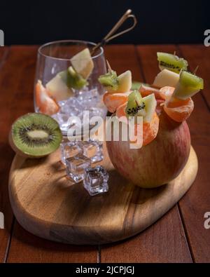 Leckere Obstspieße mit Apfel, Mandarine und Kiwi auf Holztisch Stockfoto