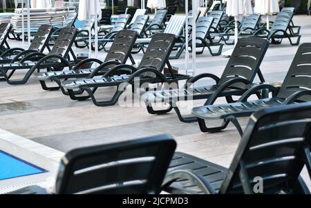 Sommerurlaub an einem sonnigen Ort. Viele Sonnenliegen am Rand des Pools. Stockfoto