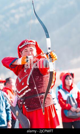 Isyk-Kul, Kirgisistan - 29. September 2018: Frau in rotem Kleid mit Pfeil in einem Bogen, der auf das Schlagen eines Ziels fokussiert ist Stockfoto