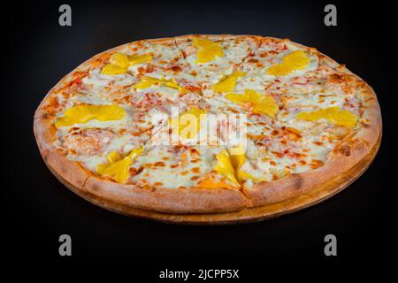 Nahaufnahme der hawaiianischen Pizza mit Ananas und Huhn auf Mozzarella-Käse auf einer dicken Kuchenkruste auf schwarzem Hintergrund Stockfoto