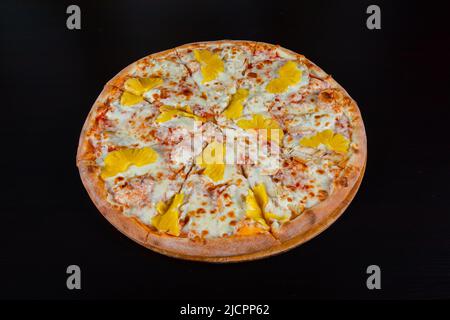 Hawaiianische Pizza mit Ananas und Huhn auf Mozzarella-Käse auf einer dicken Tortenkruste auf schwarzem Hintergrund Stockfoto