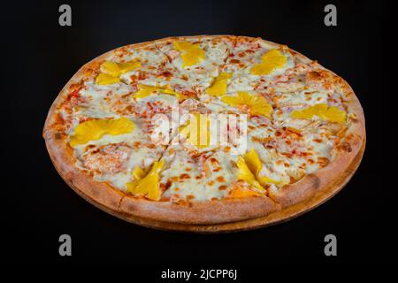 Hawaiianische Pizza mit Ananas und Huhn auf Mozzarella-Käse auf einer dicken Tortenkruste auf schwarzem Hintergrund Stockfoto