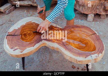 Zimmermann gießt Leinöl auf einen Holztisch. Prozess der Herstellung von Holztisch Stockfoto