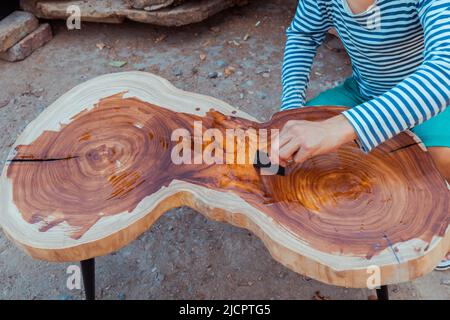 Zimmermann gießt Leinöl auf einen Holztisch. Prozess der Herstellung von Holztisch Stockfoto