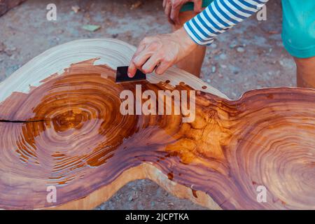 Zimmermann gießt Leinöl auf einen Holztisch. Prozess der Herstellung von Holztisch Stockfoto