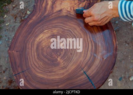 Zimmermann gießt Leinöl auf einen Holztisch. Prozess der Herstellung von Holztisch Stockfoto