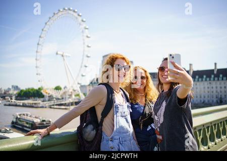 Die Menschen machen ein Selfie vor dem London Eye, während sie das sonnige Wetter auf der Westminster Bridge in London genießen. Bilddatum: Mittwoch, 15. Juni 2022. Stockfoto