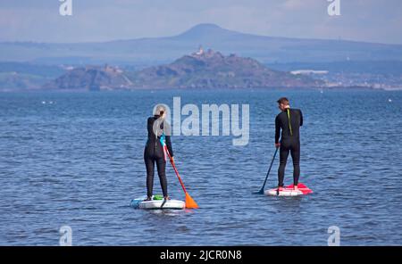 Portobello, Edinburgh, Schottland, Großbritannien. 15.06.2022. Hitzewelle verlockend die Paddlebarder auf den Firth of Forth, es ist ein paar Wochen her, dass sich irgendwelche aufgrund der jüngsten kühlen bewölkten Bedingungen gewagt haben. Die Temperatur von 18 Grad an diesem Morgen brachte einige für die Übung heraus. Im Bild: Männliche und weibliche Paddlebarder mit Inchkeith Island im Hintergrund. Kredit: Scottiscreative/alamy Live Nachrichten. Stockfoto