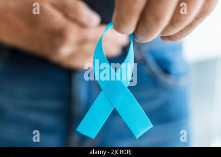Ein älterer Mann hält ein blaues Band zur Krebswahrnehmung in der Hand Stockfoto