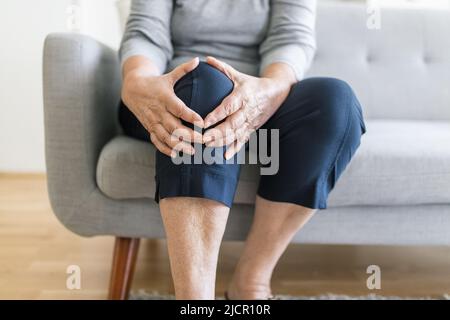 Ältere Frau sitzt auf der Bank und hält ihr schmerzhaftes Knie Stockfoto