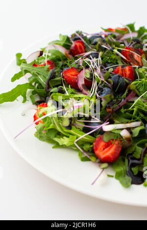 Leichter Salat mit Rucola und Beeren, Erdbeeren und Blaubeeren, köstlicher gesunder Sommersalat auf weißem Hintergrund Stockfoto