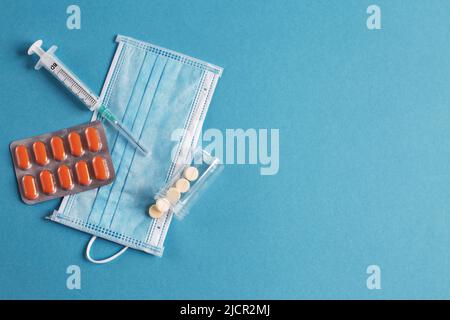 Weiße medizinische Maske, Spritze, Tabletten und Fläschchen mit Medikamenten auf der blauen Oberfläche. Coronavirus, Grippe, Konzept für Atemwegserkrankungen. Horizontale Orientatio Stockfoto