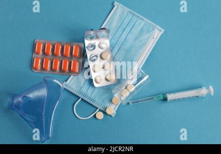 Medizinische Maske, Spritze und Tabletten schließen sich auf dem blauen Hintergrund. Coronavirus, Grippe, Konzept für Atemwegserkrankungen. Horizontale Ausrichtung. Draufsicht. Stockfoto