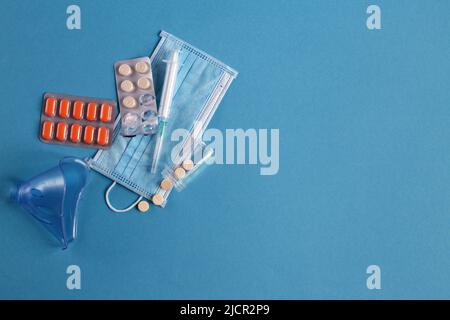 Medizinische Maske, Spritze und Tabletten schließen sich auf dem blauen Hintergrund. Coronavirus, Grippe, Konzept für Atemwegserkrankungen. Horizontale Ausrichtung. Draufsicht. Stockfoto