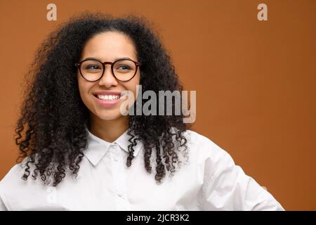 Fröhliche weibliche Youngster isoliert braune Farbe Hintergrund. Junge multirassische Frau, die lächelnd lächelt, steht in der Nähe von leerem Raum Stockfoto