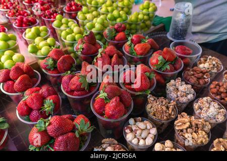 Nahaufnahme von Erdbeeren, Nüssen, getrockneten Früchten, Kirschen und Mispel in Plastikbechern. Theke mit Früchten, Beeren und getrockneten Früchten, ein touristischer Ort. Stockfoto