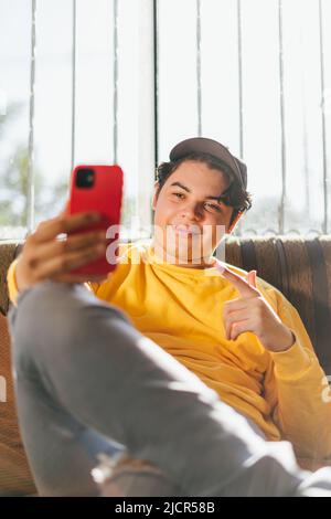 Junge Person hält sein rotes Handy und begrüßt Freunde per Videoanruf. Mann, der mit Familienmitgliedern spricht und sie glücklich begrüßt Stockfoto