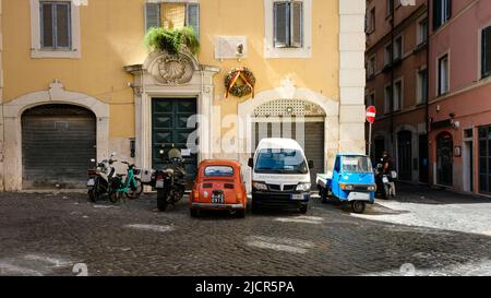 Rom, Italien - 6. Juni 2022: Fahrzeuge von kontrastierendem Typ und Farbe in Ruhe auf Kopfsteinpflasterstraße in Rom, Italien. Stockfoto