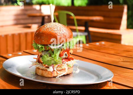 Großer, leckerer Rindfleisch-Burger oder Hamburger auf Metallplatte auf Holztisch im Straßencafe im Freien. Brunch am sonnigen Tag, Fastfood. Kopierbereich, Vorderseite Stockfoto