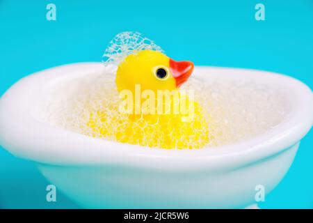 Nahaufnahme einer Gummiente in einer Miniaturbadewanne voller Seifenblasen. Badezeit-Konzept. Stockfoto