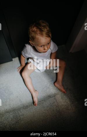 Dark High-Angle-Ansicht Porträt von traurigen anonymen kleinen Mädchen auf mfloor sitzen. Stockfoto