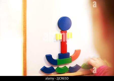 Kind spielt magnetische Holzspiel. Mädchen spielt mit einem Spielzeug auf weißem Hintergrund. Kind spielt mit einem Konstrukteur Stockfoto