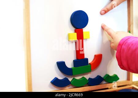 Kind spielt magnetische Holzspiel. Mädchen spielt mit einem Spielzeug auf weißem Hintergrund. Kind spielt mit einem Konstrukteur Stockfoto