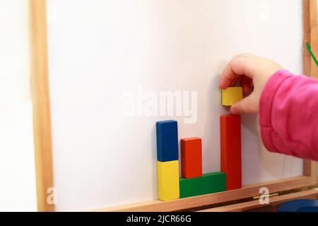 Kind spielt magnetische Holzspiel. Mädchen spielt mit einem Spielzeug auf weißem Hintergrund. Kind spielt mit einem Konstrukteur Stockfoto